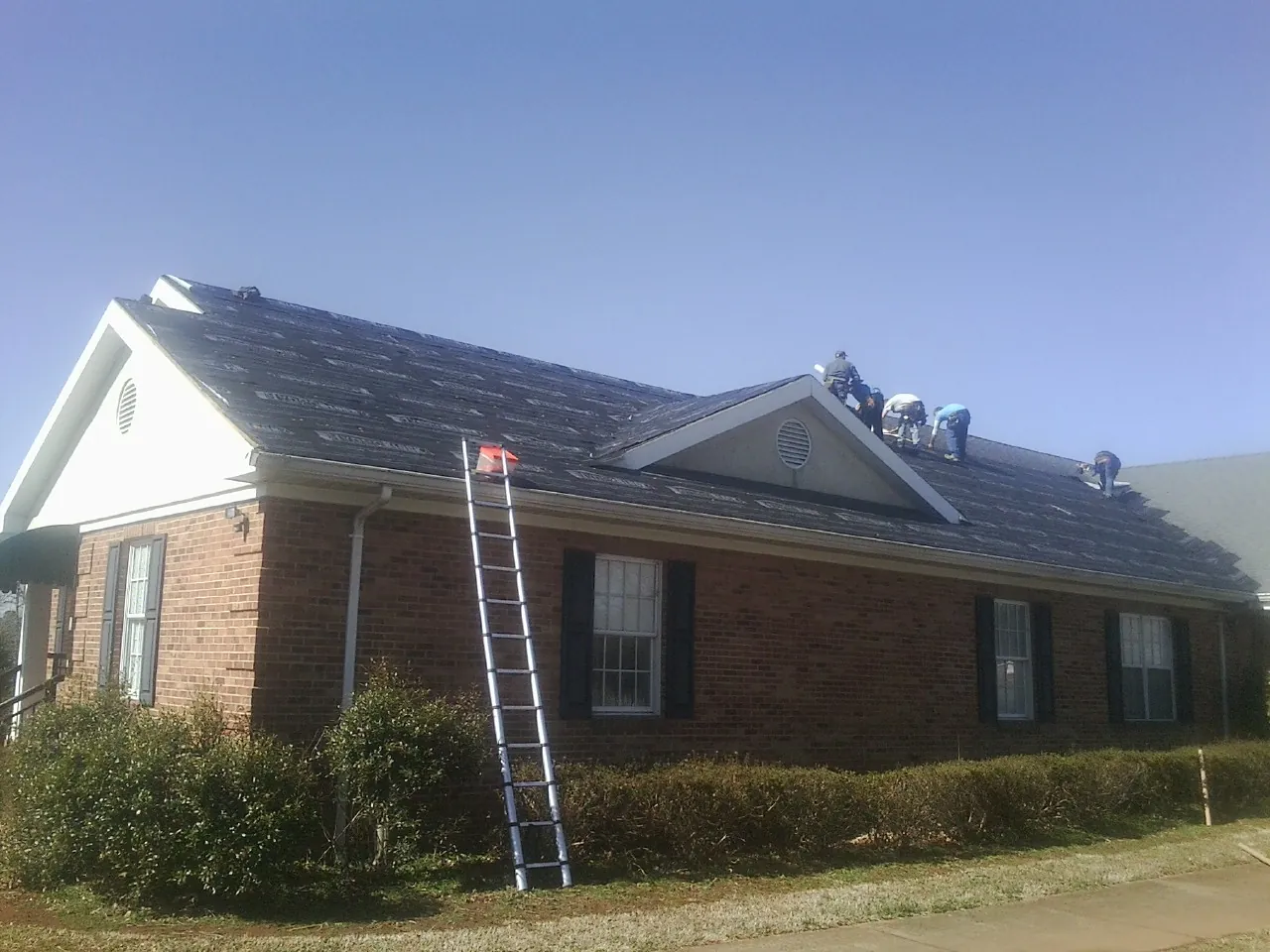 Crew tearing shingles off a brick ranch roof with a ladder set — Emergency Roof Repair work by our crew in Hauppauge