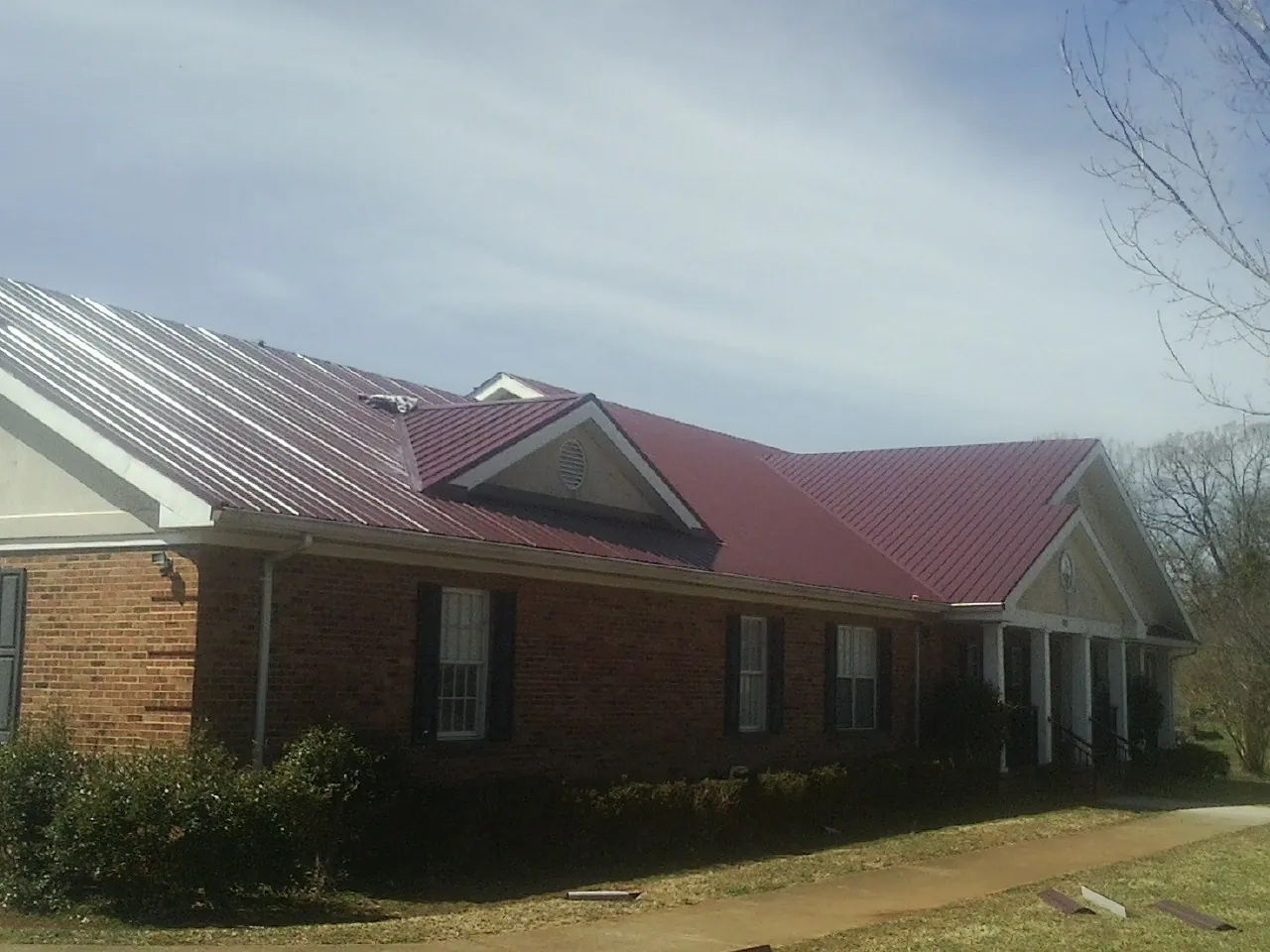 Red metal roof with gabled entries on a long brick building, from a Hail Damage Roof Repair job in Hauppauge