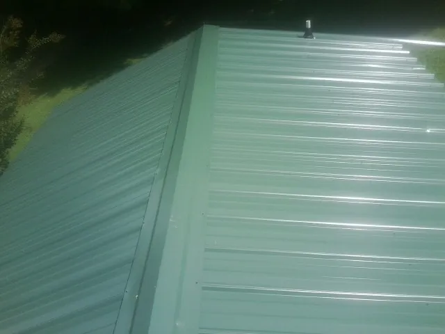 New green metal panels meeting at the ridge of a roof — Flat Roof Repair work by our crew in Hauppauge