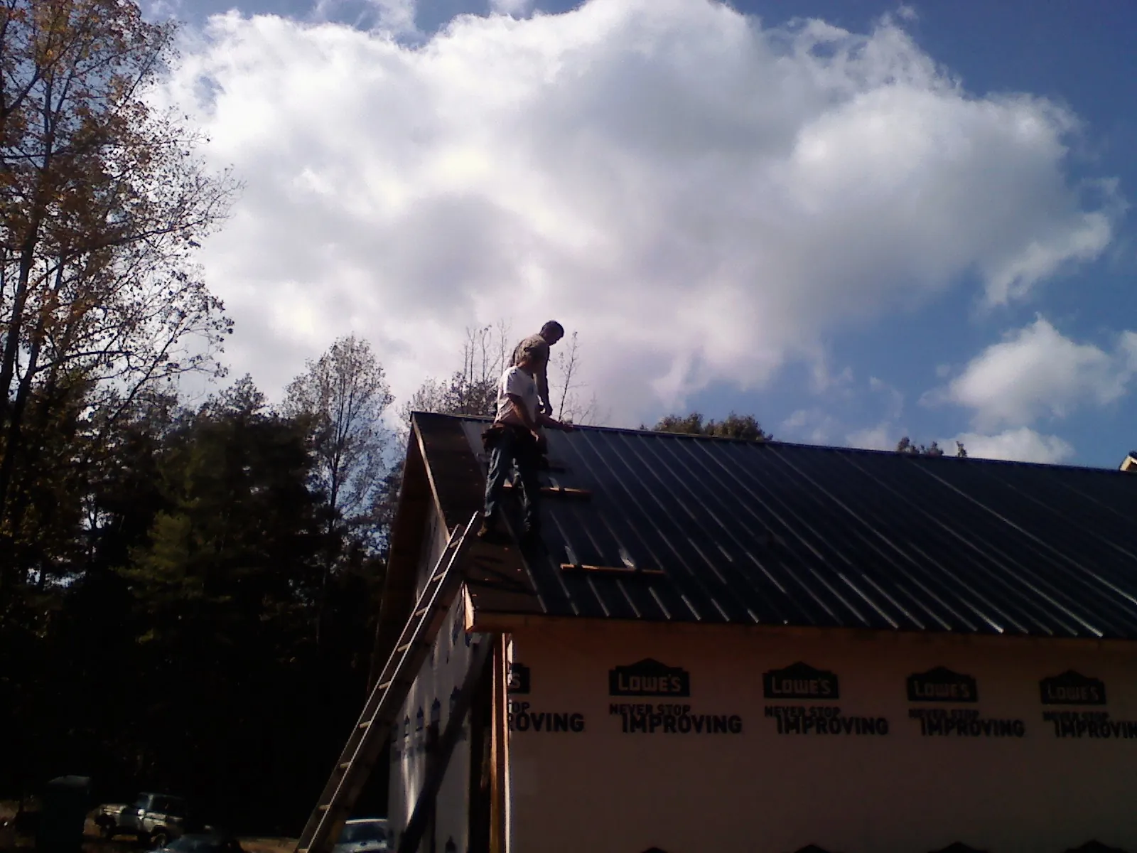 Roofer fastening dark metal panels high against a cloudy sky, from a Roof Inspection job in Hauppauge