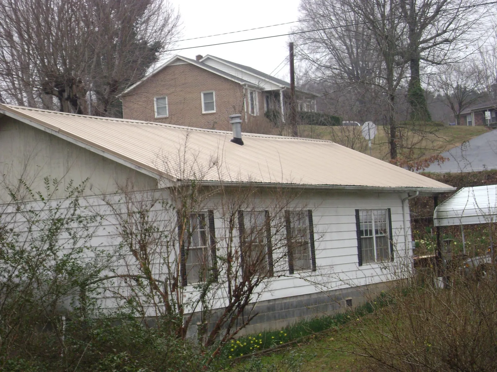 Tan metal roof on a white sided house set into a hillside — Commercial Roofing by Roofing Brothers in Hauppauge